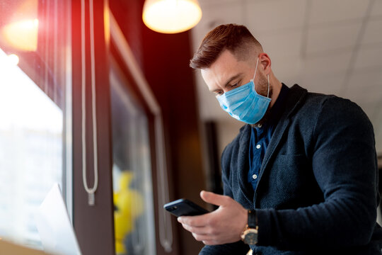 Handsome businessman in protective mask working in cafe. Man wearing a face mask and working with his phone. - Powered by Adobe