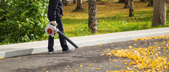 A man, a utility worker, removes leaves from the road with a special device.