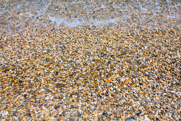 Small pebbles on the shore in a beach with wavy sea. Summer background photo.