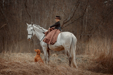 Little girl in riding habit with horse and vizsla in spring forest - 459330264