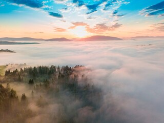 Fog spreads over the mountains at dawn. The sun rises on the horizon. Ukrainian Carpathians in the morning. Aerial drone view.