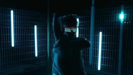 Graceful woman in futuristic glowing glasses dancing outdoors in night city with light tubes at background. Hiphop. Stylish female dancing. Youth culture. Slow motion in 4K, UHD - Powered by Adobe