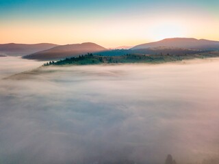Obraz premium Fog spreads over the mountains at dawn. The sun rises on the horizon. Ukrainian Carpathians in the morning. Aerial drone view.