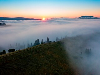 Fog spreads over the mountains at dawn. The sun rises on the horizon. Ukrainian Carpathians in the morning. Aerial drone view.