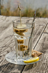 Glass of ginger tea on a saucer with a piece of lemon and a biscuit on a wooden table on a sunny day