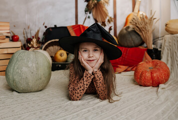 portrait of a little girl in a witch's hat lying on a knitted blanket with pumpkins