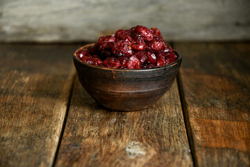 Dried cranberries in a ceramic bowl on a wooden old table.