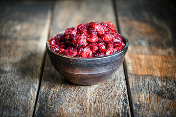Dried cranberries in a ceramic bowl on a wooden old table.