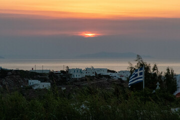 Sun Setting in the Distance Along the Water in Mykonos by a Greek Flag Flying