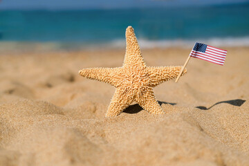 Fototapeta na wymiar A starfish holds an American flag on the seashore. Labor day holiday concept. 4th of July USA Independence Day. Copy space for text.