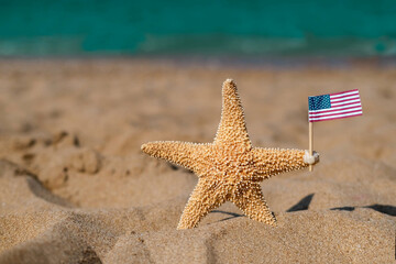 A starfish holds an American flag on the seashore. Labor day holiday concept. 4th of July USA Independence Day.  Copy space for text.