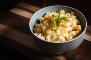 Mac and cheese with basil on top on a rustic wooden board