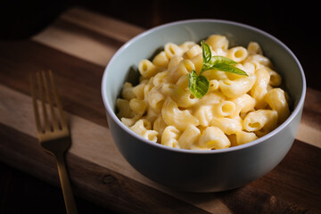 Mac and cheese with basil on top on a rustic wooden board