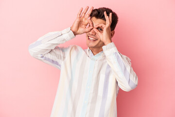 Young caucasian man isolated on pink background showing okay sign over eyes