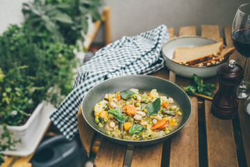 A plate with tasty italian soup minestrone on wooden table outddors in the garden