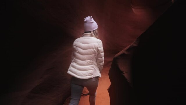 Camera follows woman on trip or adventure. Young millennial traveller or travel blogger walk in beautiful cinematic red and orange wavy pattern Antelope canyon. Generation z new concept travels USA 4K