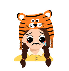 Girl with big eyes and depressive emotion, crying, tears face in tiger hat. Cute kid with sad face in a festive costume for New Year, Christmas and holiday. Head of adorable child with emotions