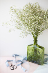 Preparing the bouquet for the wedding ceremony, a bouquet of white gypsophila flowers stands in a green vase along with ribbons and scissors.