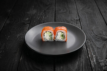 Japanese cuisine. Rolls on a round plate on a black table.
