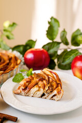 Slice of delicious apple cake on kitchen table with apples and leaves on background