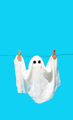 Laundry or sheets ghost hanging on the rope with spooky eyes behind sky blue vivid background. Minimal Halloween fun idea.