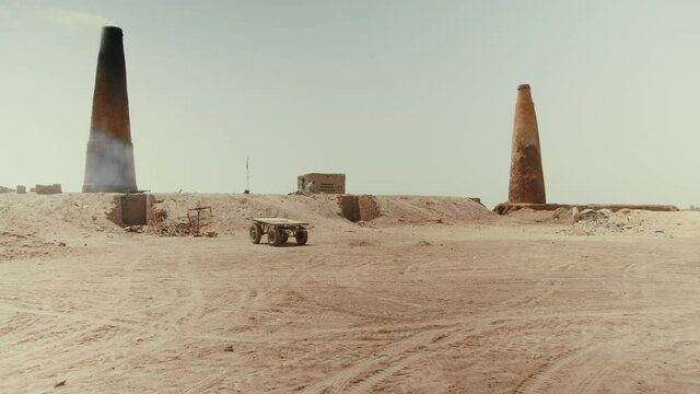 A brick factory in Pakistan that uses slave labor. On the sand there is an empty trailer. Against the background of the pipe from which there is smoke