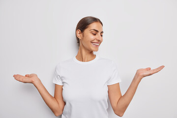 Horizontal shot of pleased young European woman faces difficult choice spreads palms pretends...