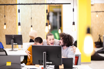 Three caucasian colleagues cheering for job well done in a modern office with decorative hanging lightbulbs.