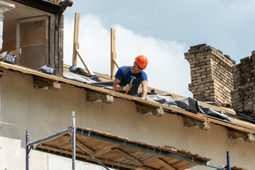 Repair of a wooden roof outdoors on a summer day against the background of blue sky and clouds. A...
