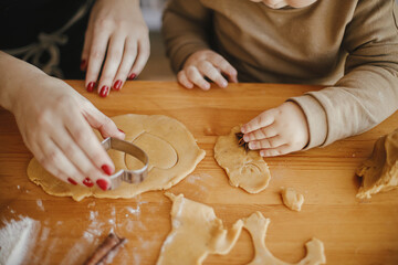 Cute daughter and mother making together christmas cookies on messy table. Adorable toddler girl helper with mom cutting dough for gingerbread cookies. Family preparations for xmas holidays