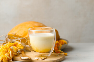 A glass of vegetable milk made from pumpkin seeds and turmeric. Close-up, sliced pumpkin in the background. Horizontal, copy of the space