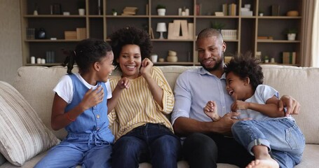 Cheery African family tickling each other laughing having fun enjoy playtime sit together on cozy sofa at modern living room. Bank loan mortgage, happy homeowners, leisure with children, love concept - Powered by Adobe