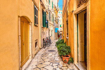 Fototapeta na wymiar Kerkyra city narrow street view with yellow colorful houses and bikes during sunny day. Corfu Island, Ionian Sea, Greece.