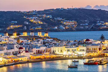 Chora port of Mykonos island with famous windmills, ships and yachts during colorful sunset. Aegean...