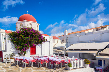 Famous old town narrow street with white houses, Bougainvillea flower and red church. Mykonos island, Greece
