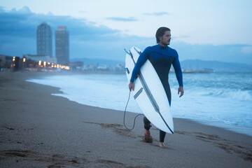 Young surfer holding surf board and walking along the coast, ready for surfing at Barcelona beach