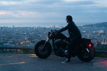 From the back shot of biker or moto rider after sunset, doing his trip ride with beautiful city and...