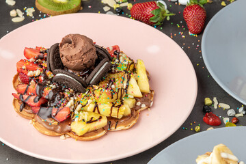 Heart waffle with pineapple and strawberry with gummy candy and ice cream on it.