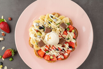 Heart waffle with banana and strawberry with gummy candy and ice cream on it.