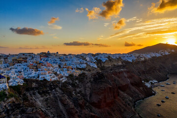 Aerial drone view of famous Oia village with white houses and blue dome churches during sunrise on Santorini island, Aegean sea, Greece.