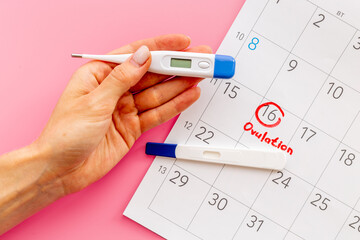 Female hand with thermometer over calendar basal temperature