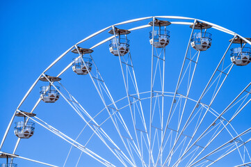Detail of a white ferris wheel with empty cabins against a cloudless blue sky