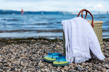 wicker basket, towel and slippers on a rocky beach against a beautiful sky