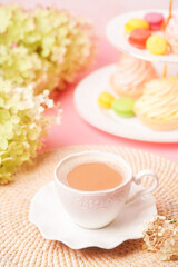 Fototapeta na wymiar a white cup of coffee with sweets and a bouquet of flowers in soft, pastel colors. Congratulations on your birthday or mother's day. Close up