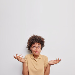 Indecisive hesitant curly young African American woman spreads palms feels doubtful focused above...