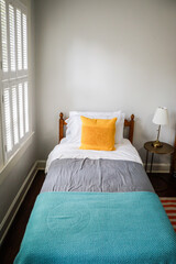 A guest bedroom with a single twin bed with turquoise and gray bedspread and yellow decorative...