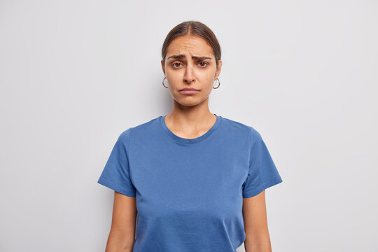 Displeased sulking woman has sad frustrated face expression raises eyebrows feels disappointed wears casual blue t shirt isolated over white background. Bothered distressed young female model