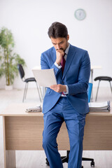 Young male employee reading paper at workplace