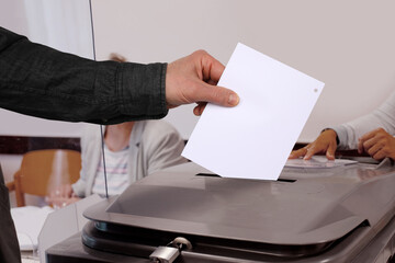 male voter throws a ballot paper into a gray ballot box at a polling station in Germany, hand with...