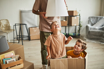 Portrait of two cheerful boys playing in big cardboard box while family moving to new house, copy space - obrazy, fototapety, plakaty